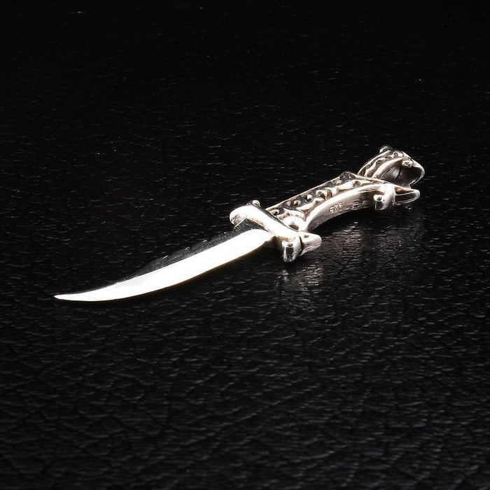 The sterling silver dagger pendant at an angle, full length, with mirror-polished curved blade and ornate scroll hilt.