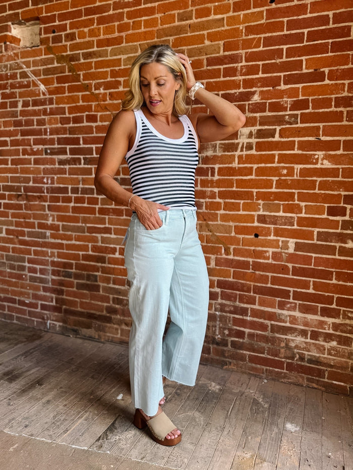 Model wearing wide leg crop jeans in Winter Sky with striped tank and sandals.