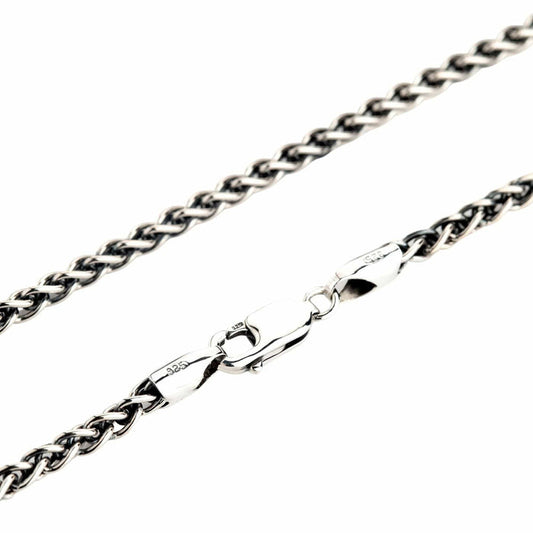 A close-up of a solid sterling silver wheat chain necklace, showing the intricate braided links and the secure lobster clasp.