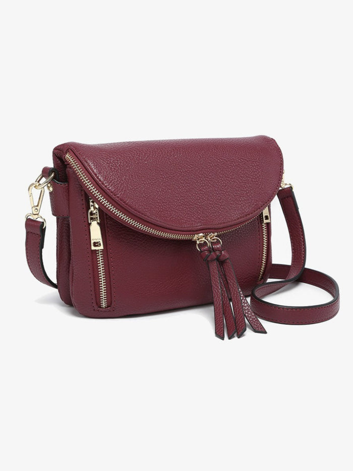 A burgundy pebbled leather crossbody bag with gold-tone hardware, featuring a front flap, two zippered pockets, and a matching leather tassel detail, shown on a light gray background.