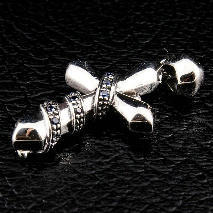 Low angle view of the polished silver cross on black leather, highlighting the prominent bail and blue CZ chain wrap.