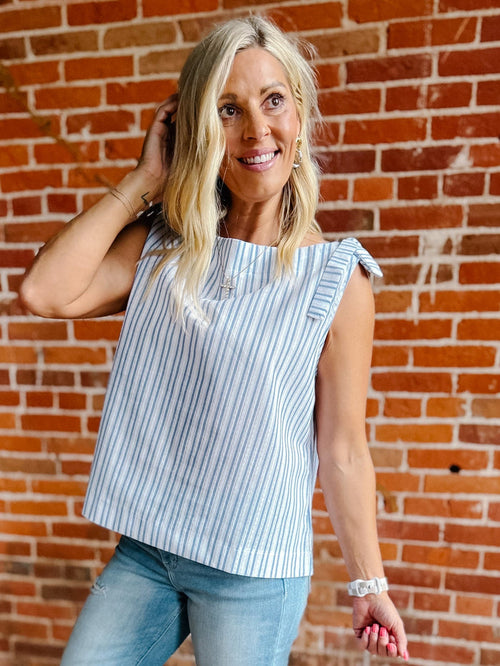 A woman wearing a blue and white vertical striped tank top with shoulder ties and a ruched neckline.