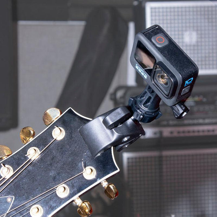 A GoPro camera with the Clamp Mount with GoPro Mount is attached to a guitar’s headstock, while amplifiers and music equipment appear softly blurred in the background.