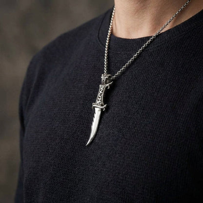 Man in a black knit shirt wearing the curved silver dagger pendant on a chain, blade pointing down, scroll hilt on top.