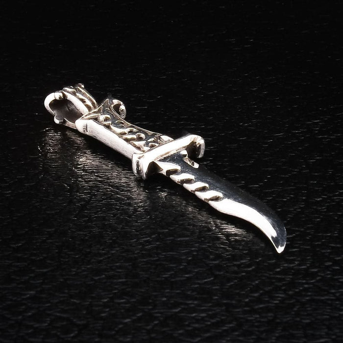 Angled view of the sterling silver dagger pendant — polished curved blade, notched spine, and openwork scroll hilt.
