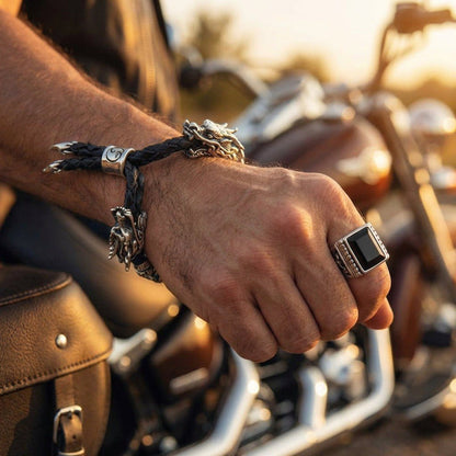 Sterling silver dragon head bracelet with black braided leather and claw pendants worn on biker's hand beside motorcycle saddlebag