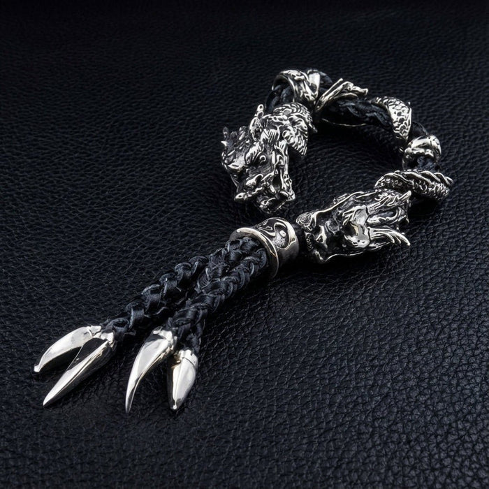 Overhead view of coiled black braided leather bracelet with silver dragon head beads and four polished claw pendants fanning outward