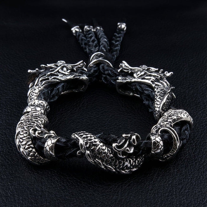 Two detailed 925 silver dragon bodies coiling around black braided leather with tassel ends fanning at top
