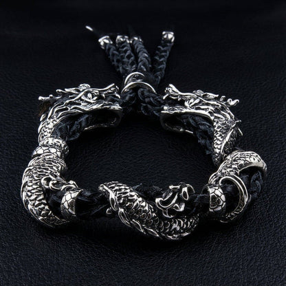 Two detailed 925 silver dragon bodies coiling around black braided leather with tassel ends fanning at top
