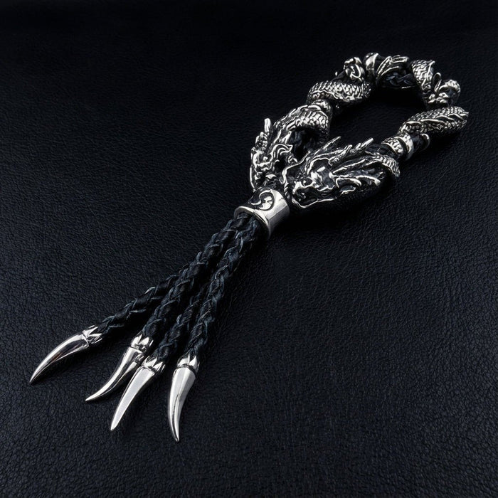 Three polished sterling silver claw tips at base of black braided leather tassel beneath coiled dragon bracelet