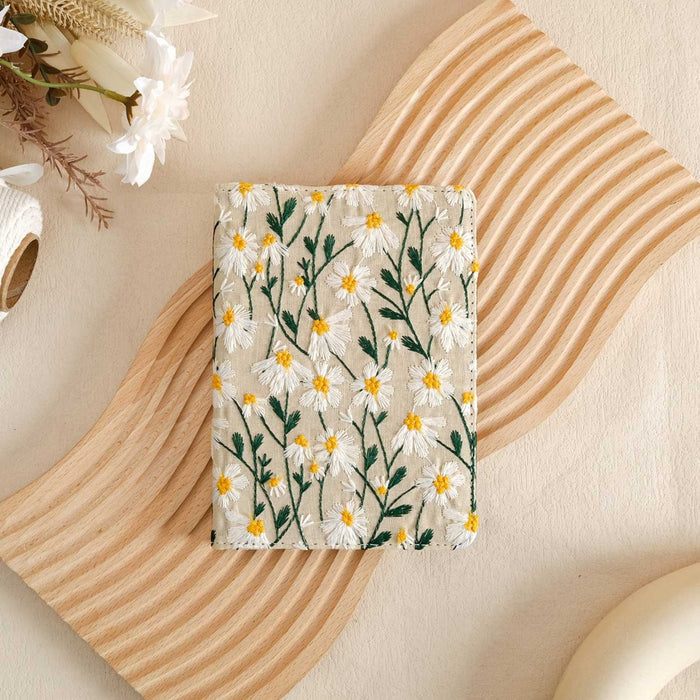 A white vegan leather Kindle case with a floral pattern, displayed on a wooden surface with a Kindle and a cup.