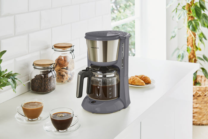 Filter coffee maker on a kitchen counter with two cups of coffee and jars of coffee beans.