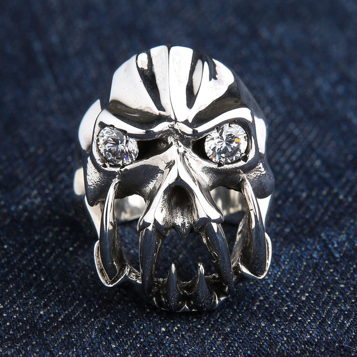 A front view of the heavy sterling silver fang devil ring with clear diamond CZ eyes, resting on a denim background.