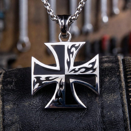 Sterling silver Iron Cross pendant necklace with tribal flame design on black enamel, displayed on black leather with workshop tools in the background