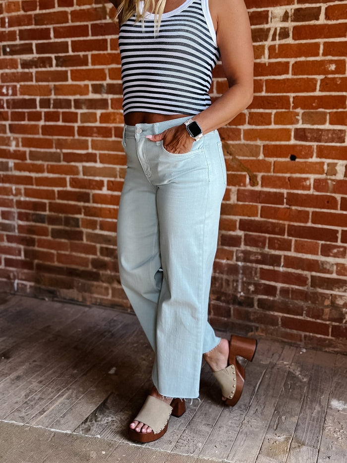 Model wearing wide leg crop jeans in Winter Sky with striped tank and sandals.