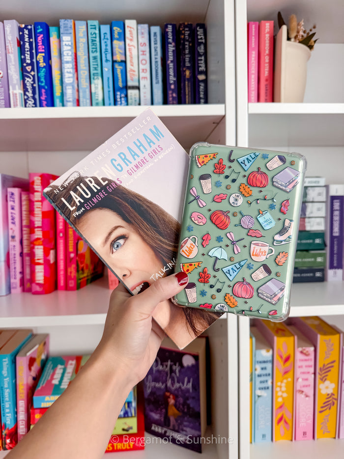 Hand holding a gilmore girls kindle case in front of a bookshelf filled with books
