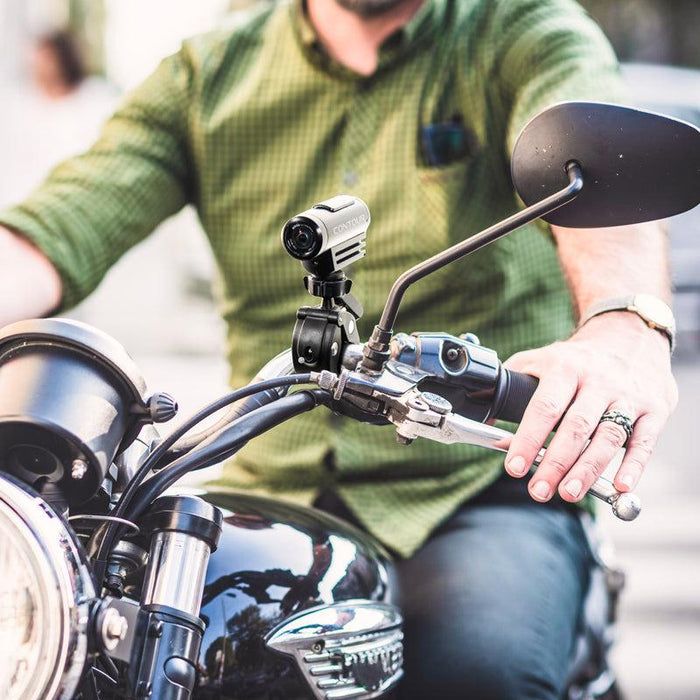 A rider in a green checkered shirt grips the handle of a black motorcycle equipped with the Handlebar Clamp Camera Mount, highlighting the mount and the rider’s hand.