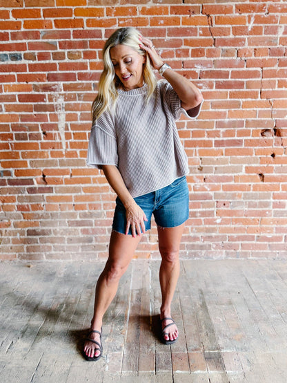 Woman wearing a soft knit sweater with exposed seams and short sleeves, standing against a brick wall.