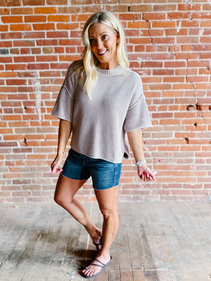 Woman wearing a soft knit sweater with exposed seams and short sleeves, standing against a brick wall.