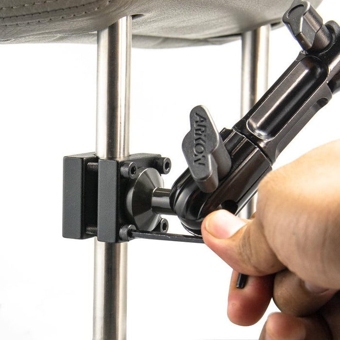 A hand tightens the Heavy Duty Aluminum Car Headrest Mount with 4-Hole AMPS Head onto a metal rod using an Allen wrench, securing a sturdy backseat entertainment setup.