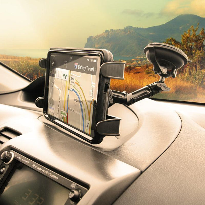 A car dashboard features a smartphone with GPS navigation, mounted using the Heavy-Duty Multi-Angle Slim-Grip® Tablet Suction Mount with 8 Arm; mountains and trees are visible through the windshield under a cloudy sky.