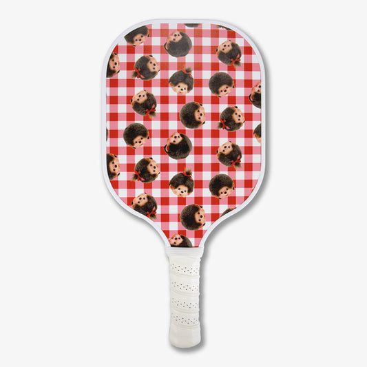Front view of Monchhichi pickleball paddle with red-and-pink gingham pattern of repeating Monchhichi faces and white wrapped handle