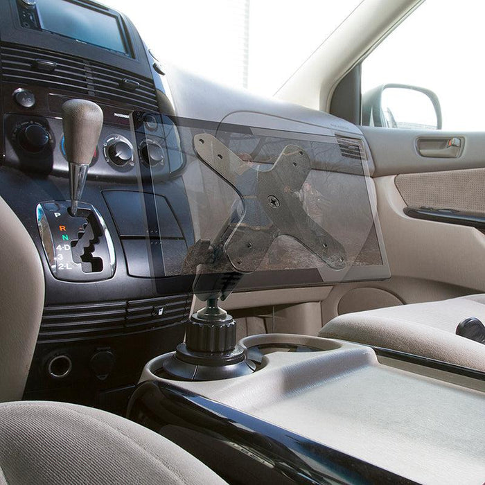 A Heavy-Duty Car Cup Holder VESA Mount is installed near the center console between the driver and passenger seats, with the dashboard, gear shift, and cup holders visible. No tablet is mounted.