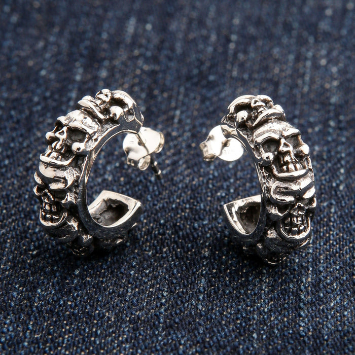 A pair of men's sterling silver multi-skull hoop earrings with a post and butterfly back, resting on blue jeans.