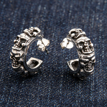 A pair of men's sterling silver multi-skull hoop earrings with a post and butterfly back, resting on blue jeans.