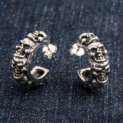 A pair of men's sterling silver multi-skull hoop earrings with a post and butterfly back, resting on blue jeans.
