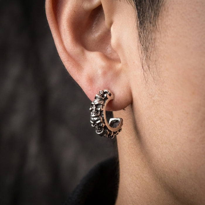 Close-up of a model wearing a silver multi-skull hoop earring on their ear, showcasing the detailed gothic biker design against a dark textured background.