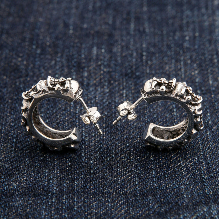 A close-up macro shot of the detailed, individually carved skulls on the sterling silver hoop earring.