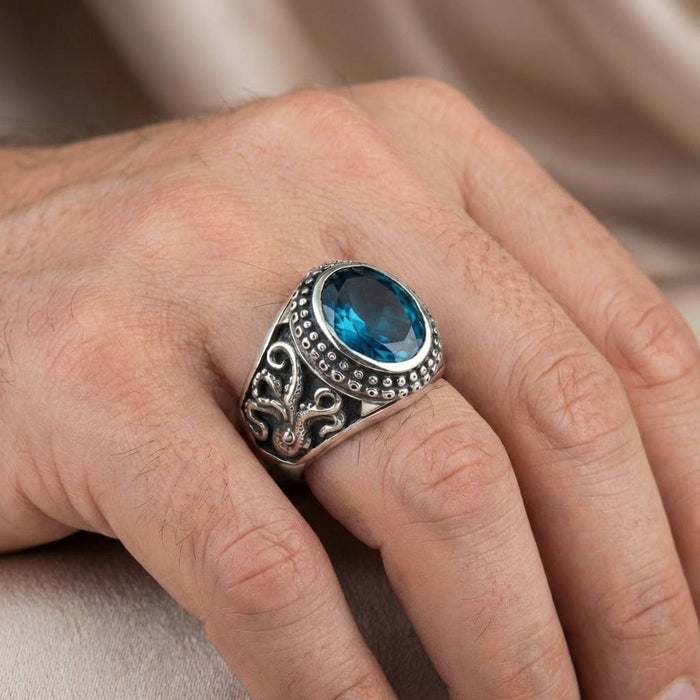 Sterling silver octopus ring with oval blue topaz gemstone worn on a man's hand, featuring detailed tentacle engravings and beaded border design in vintage biker style