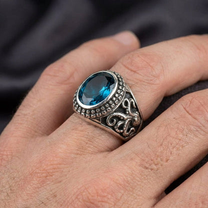 Sterling silver octopus ring with oval blue topaz gemstone worn on a man's finger, featuring detailed tentacle design on the band and beaded bezel setting