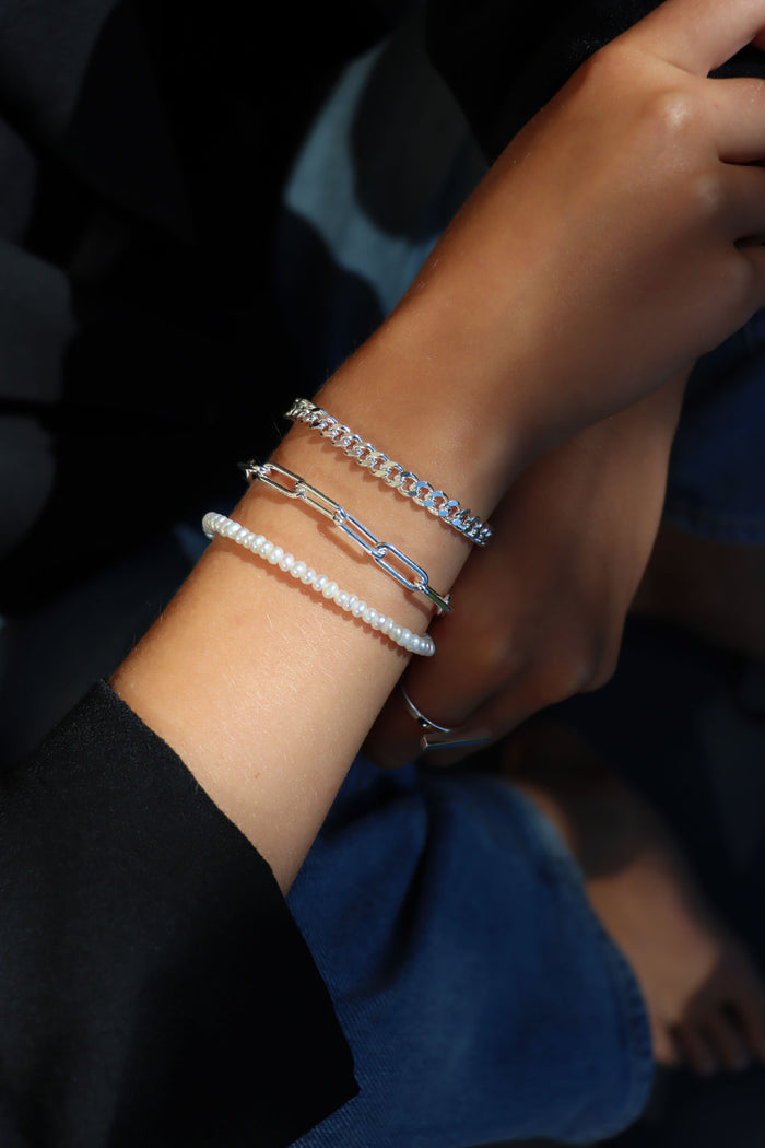 Tjej som bär tre armband, armband med silverkedjor och pärlarmband.