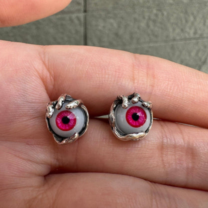 Pair of red glass evil eye stud earrings held by sterling silver claws, resting on an open palm.