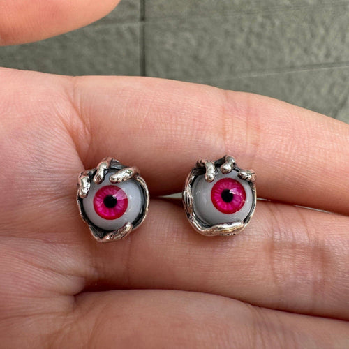 Pair of red glass evil eye stud earrings held by sterling silver claws, resting on an open palm.