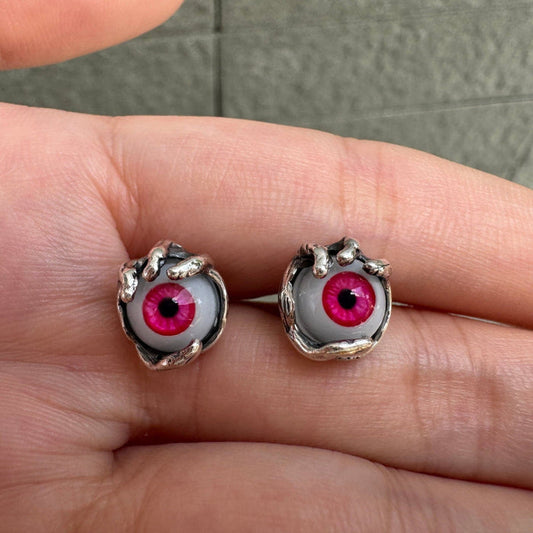 Pair of red glass evil eye stud earrings held by sterling silver claws, resting on an open palm.
