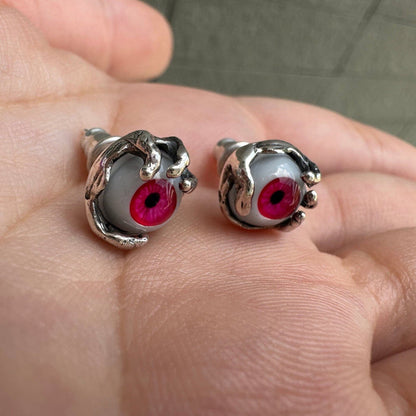 Angled display of two red glass dragon eye studs on a palm, showcasing the textured silver claws and back posts.