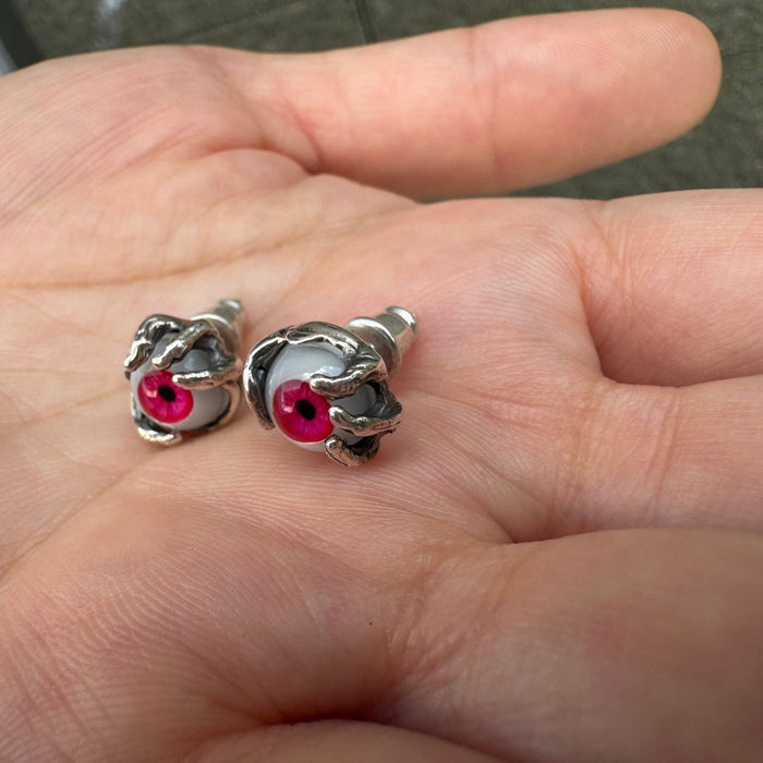Lying in a palm, two red glass eyeball earrings reveal the depth of their sterling silver claw settings and back posts.