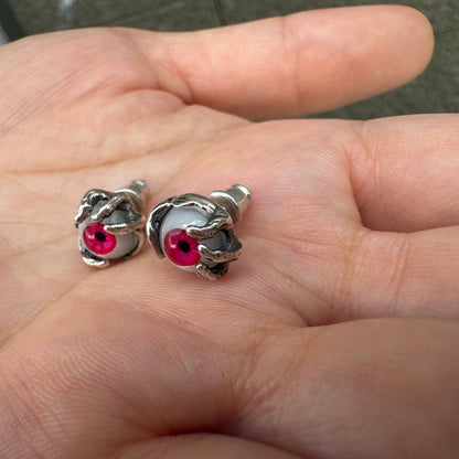 Lying in a palm, two red glass eyeball earrings reveal the depth of their sterling silver claw settings and back posts.