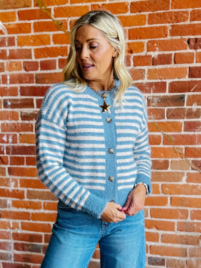 A woman wearing a striped fuzzy cardigan in dusty blue and white, buttoned up with ribbed hem and cuffs.