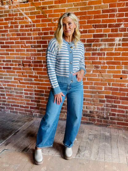 A woman wearing a striped fuzzy cardigan in dusty blue and white, buttoned up with ribbed hem and cuffs.