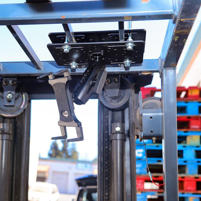 A close-up of the Slim-Grip® Overhead Guard Forklift Tablet Mount with 5 Shaft installed on a forklift, with colorful plastic pallets stacked in the background.