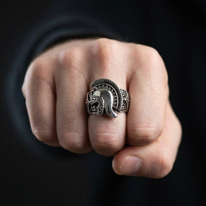 Silver Spartan Roman helmet ring with intricate tribal engravings worn on a man's middle finger, displayed on a clenched fist against a dark black background
