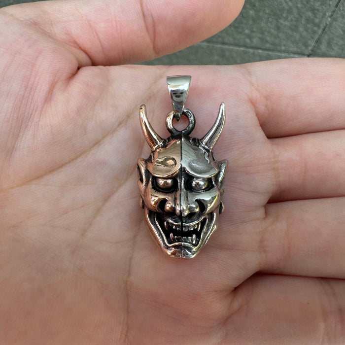 A front view of the two-tone Oni mask pendant, showcasing the split sterling silver and copper face.