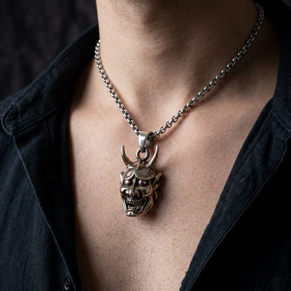Male model wearing a silver two-tone Oni mask pendant necklace with an open black shirt.