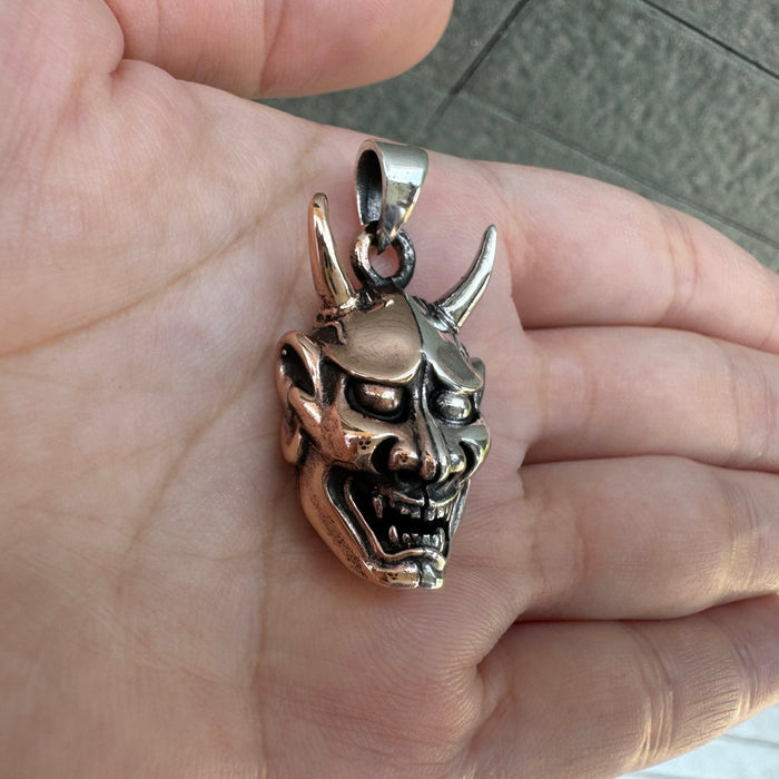 An angled view of the Japanese demon mask pendant, highlighting the menacing expression and sharp horns.