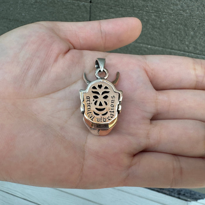 The back of the silver and copper Oni mask pendant, showing the openwork carvings and details.