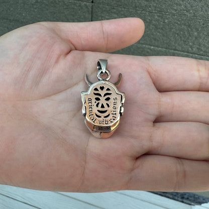 The back of the silver and copper Oni mask pendant, showing the openwork carvings and details.